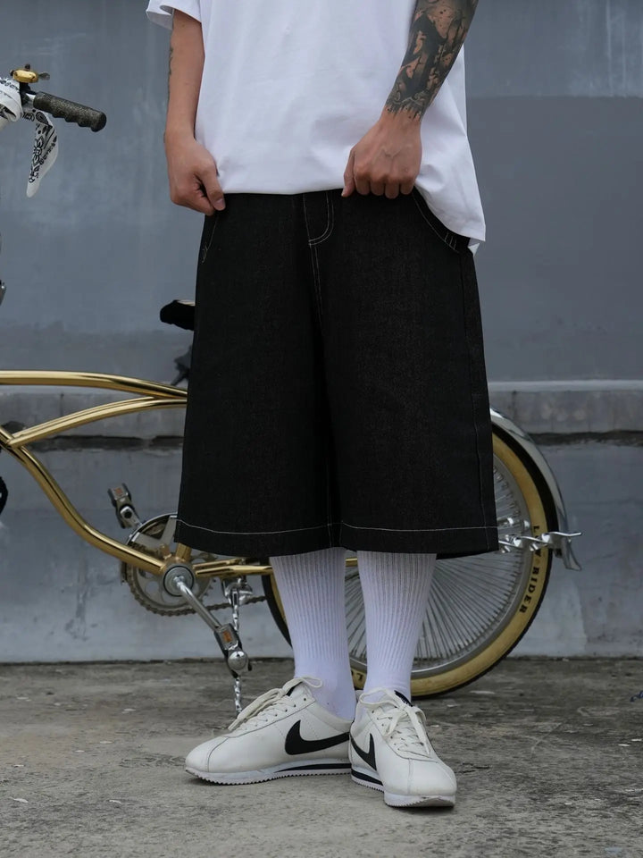 A model wearing the black Embroidery Pockets Oversized Jorts in a gray background