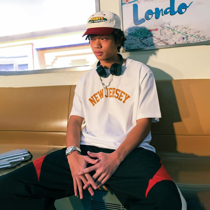 A model sitting while wearing the white New Jersey Letter Print T-shirt  from DAXUEN.