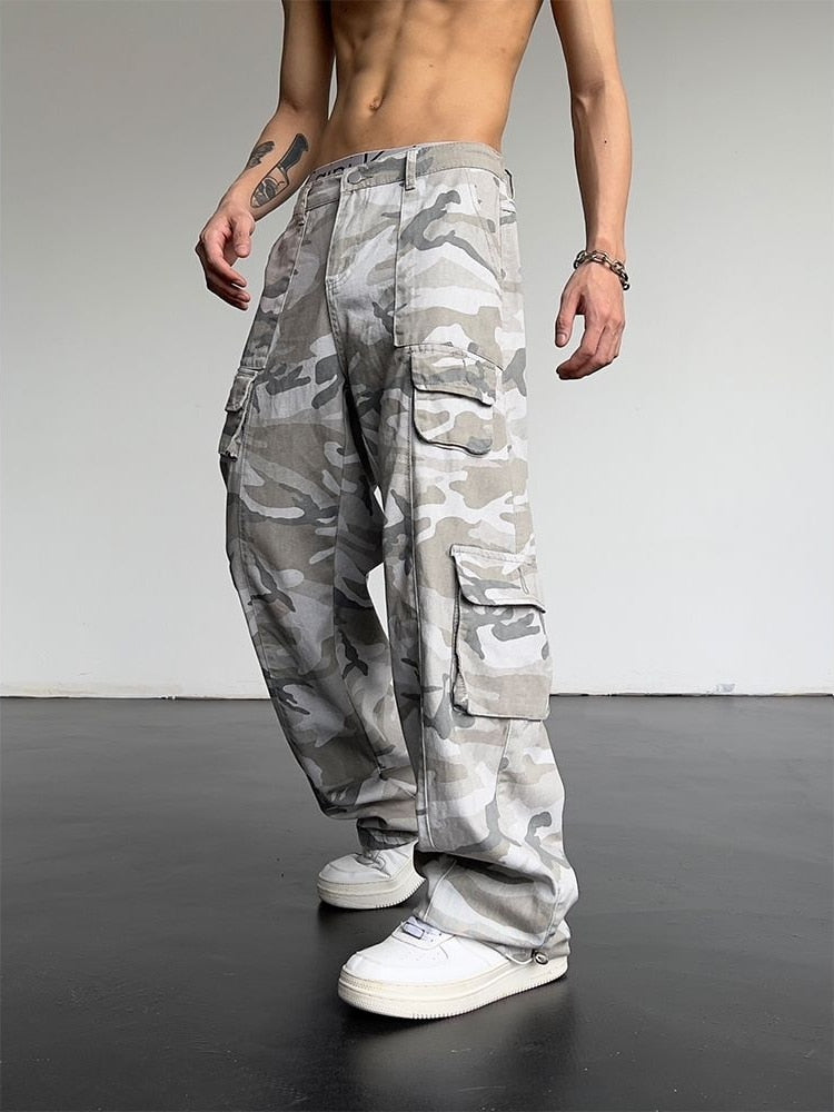 A man wearing a camo cargo pants and white sneakers in a gray background with accessories.