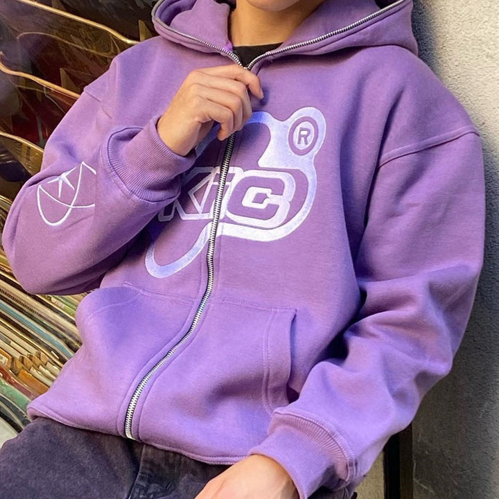A model posing while wearing the purple Y2K Loose Hoodie as well as holding the zipper