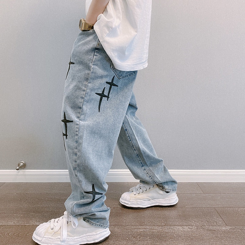 White shirt, light blue jeans with black crosses, white sneakers, wooden floor background.